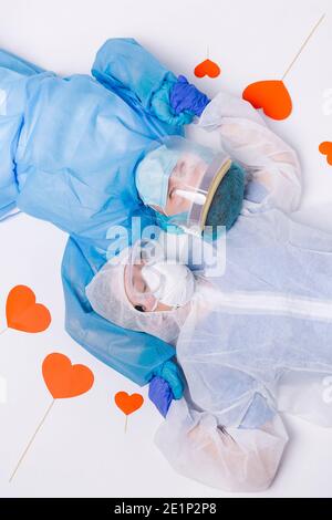 San Valentino in ospedale. Due medici in covid 19 indumenti protettivi giacenti sul pavimento con cuori rossi intorno. Foto Stock