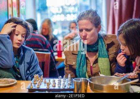 Una donna e i bambini si siedono insieme in un ristorante che studia scacchi scheda Foto Stock