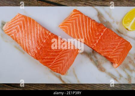 Filetto di salmone crudo con fette di limone su marmo scheda Foto Stock