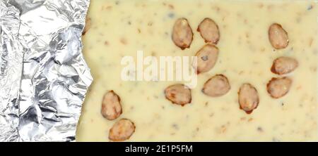 Pezzi di cioccolato bianco con pistacchi e mandorle isolati su sfondo bianco. Barretta di cioccolato bianca in un involucro di lamina aperto Foto Stock