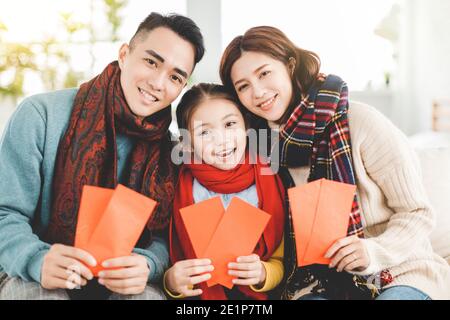 felice anno nuovo cinese. famiglia asiatica mostrando busta rossa per la fortuna in soggiorno Foto Stock