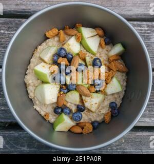 Porridge di farina d'avena con mirtilli, mandorle e mela in una ciotola da campeggio su un tavolo di legno Foto Stock