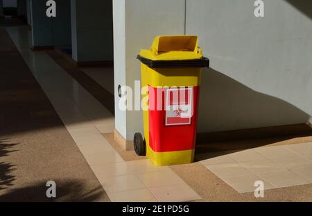 Bidone per rifiuti a rischio biologico su pavimento piastrellato contro parete blu sotto la luce del sole Foto Stock