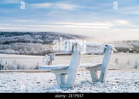 Paesaggio montano invernale e panca ghiacciata in legno al mattino Foto Stock