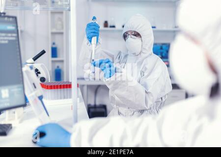 Medico sanitario che preleva il campione dalla provetta utilizzando una micropipetta. Gruppo di microbiologi in laboratorio di ricerca che conduce esperimenti durante la pandemia globale con covid19. Foto Stock