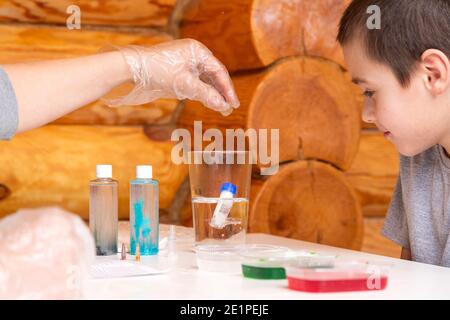 Concetto di educazione e formazione chimica. Una donna getta una provetta con un elemento chimico in un bicchiere di acqua bollente per creare un reactus chimico Foto Stock