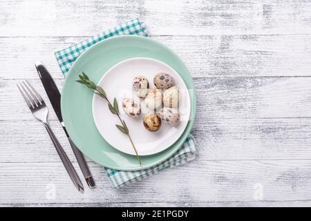 Piatto di menta bianco e verde con uova di quaglia e posate su sfondo di legno. Composizione pasquale. Spazio di copia. Vista dall'alto - immagine Foto Stock