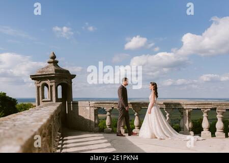 La sposa e lo sposo vanno a incontrarsi sulla terrazza del palazzo contro il cielo Foto Stock