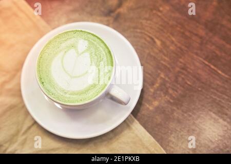 Tazza di latte matcha su sfondo di legno e un tovagliolo beige in un caffè con spazio per le copie. Foto di alta qualità Foto Stock