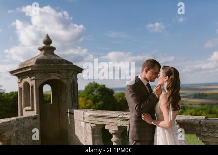 La sposa e lo sposo baciano sulla terrazza del palazzo contro il cielo Foto Stock