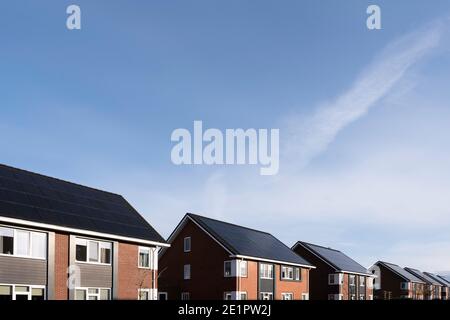 Pannelli solari montati sui tetti di una fila moderne case di nuova costruzione a Lemmer, Frisia, Paesi Bassi con cielo blu Foto Stock