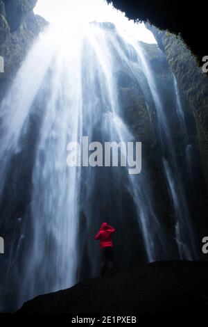 Giacca rossa in piedi sulla roccia a Gljufrabui Gljufrofoss nascosto Cascata grotta canyon dweller scogliera vicino Seljalandsfoss Sud Islanda Europa Foto Stock