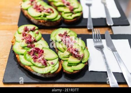 Toast di avocado con prosciutto iberico su tavole di ardesia con posate pronte per essere servite. Foto Stock