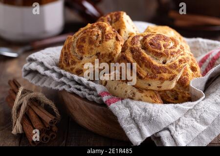 Panini alla cannella freschi in una ciotola e bastoncini alla cannella un tavolo di legno Foto Stock