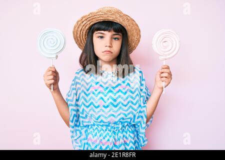 Giovane bambina con bang indossare abito estivo mangiare caramelle depressa e preoccupazione per angoscia, piangendo arrabbiato e impaurito. Espressione triste. Foto Stock