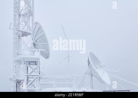 antenne paraboliche ghiacciate e il seminterrato della torre di celle a reticolo sulla stazione radio di base situata nelle alture Foto Stock