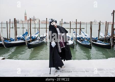 Un uomo che indossa un costume da carnevale davanti alle gondole vestite di neve, Venezia Italia Foto Stock