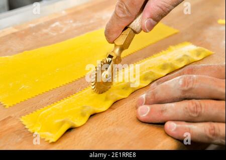 Ravioli del plin, pasta tipica delle Langhe, Piemonte, Italia - taglio a mano con coltello rotante di agnolotti su tagliere in legno Foto Stock