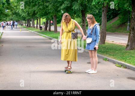 donna in piedi su longboard sostenuta da sua figlia. Donna che impara a skateboard all'aperto. Foto Stock