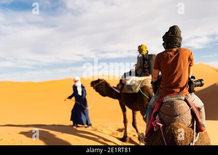 (Fuoco selettivo) vista mozzafiato di due persone che cavalcano cammelli sulle dune di sabbia a Merzouga, Marocco.