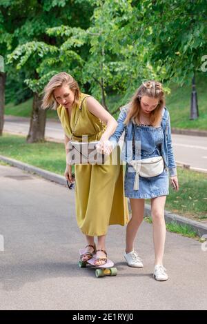 famiglia in una passeggiata nel parco. figlia insegna mamma a skateboard. Foto dello stile di vita all'aperto in una giornata estiva soleggiata. Foto Stock