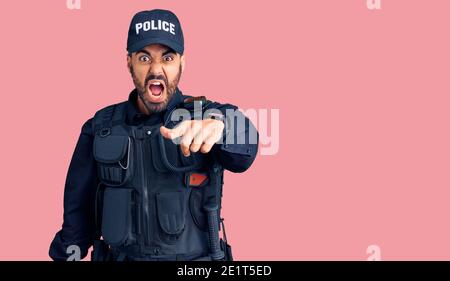 Giovane uomo ispanico che indossa uniforme di polizia che indica dispiaciuto e frustrato alla macchina fotografica, arrabbiato e furioso con voi Foto Stock