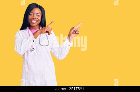 Giovane donna afroamericana indossando stetoscopio medico sorridente e guardando la macchina fotografica puntando con due mani e dita a lato. Foto Stock