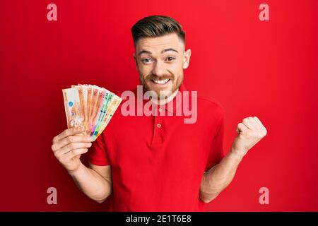 Giovane redhead che tiene le banconote del peso filippino urlando fiero, celebrando la vittoria ed il successo molto eccitati con il braccio sollevato Foto Stock