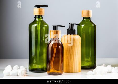 Set di bottiglie cosmetiche in vetro verde e marrone con pompe ed elementi in legno per la ricarica di prodotti di bellezza. Accessori da bagno minimalistici Foto Stock