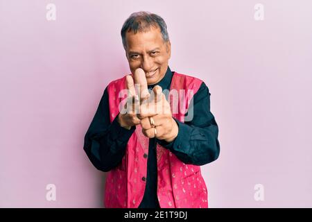 Uomo indiano di mezza età che indossa abiti indiani tradizionali puntando le dita alla macchina fotografica con viso felice e divertente. Buona energia e vibrazioni. Foto Stock