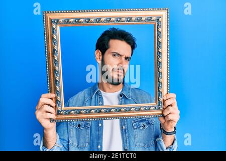 Giovane uomo ispanico che tiene vuoto cornice indistensato e confuso espressione. Dubbio concetto. Foto Stock