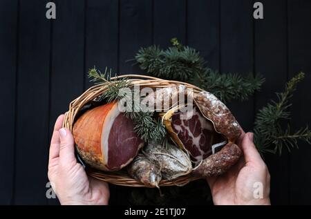 Cesto con salame, coppa e prosciutto su fondo di legno scuro. Specialità italiane. Decorazioni natalizie. Foto Stock