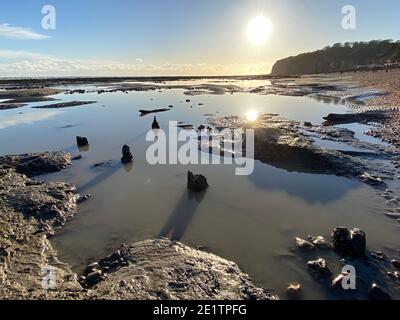 Spiaggia di Pett Level al tramonto. Con piscina di acqua marina e rocce in primo piano. Winchelsea Beach incontra le scogliere, una foresta pietrificata visibile in basso Foto Stock