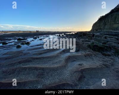 Spiaggia di Pett Level al tramonto. Con piscina di acqua marina e rocce in primo piano. Winchelsea Beach incontra le scogliere, una foresta pietrificata visibile in basso Foto Stock