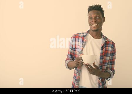 Studio shot di giovani felici Africano nero uomo sorridente tenendo tazza da caffè contro uno sfondo bianco Foto Stock