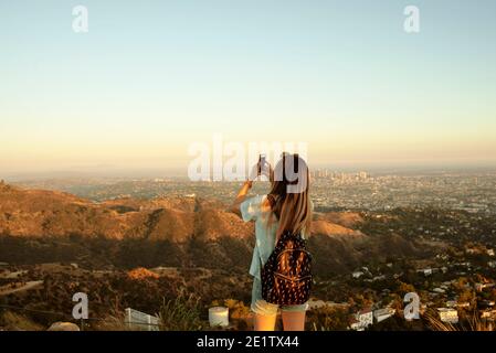 Vista posteriore della ragazza che scatta foto mobili della vista. The Hollywood Sign, Los Angeles, California, Stati Uniti. Ago 2019 Foto Stock