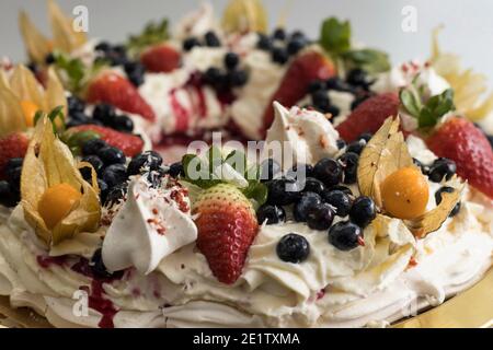 Deliziosa torta pavlova con meringa francese e panna montata, decorata con fragole, mirtilli e fisalis Foto Stock