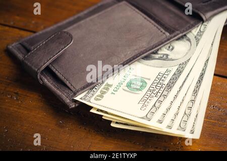 Portafoglio in pelle pieno di denaro su tavolo di legno - cento banconote USA con ritratto del presidente Franklin. Contanti di cento fatture del dollaro, valuta della carta Foto Stock