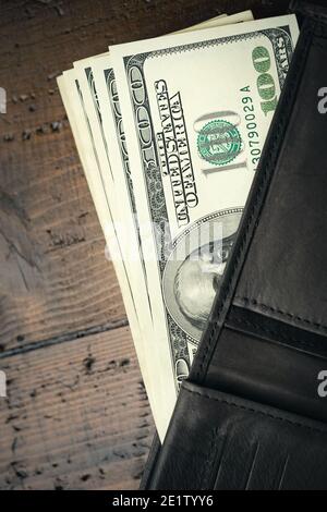 Portafoglio in pelle pieno di denaro su tavolo di legno - cento banconote USA con ritratto del presidente Franklin. Contanti di cento fatture del dollaro, valuta della carta Foto Stock