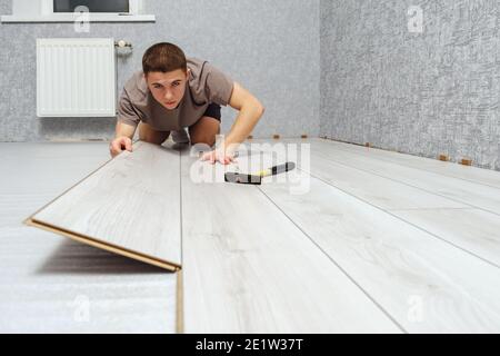 Giovane uomo di riparazione sta ponendo pannello di pavimento laminato all'interno. Foto Stock