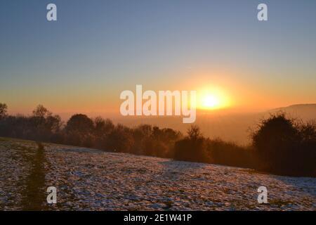 Tramonto spettacolare in luce invernale nebbiosa nel North Downs, Fackenden Down, nel Kent, vicino Sevenoaks, croccante, cielo limpido sopra un enorme bagliore arancione, cielo blu Foto Stock