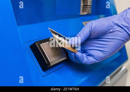 La mano di una persona in un guanto medico protettivo applica una carta bancaria al terminale e paga senza contatto. Foto Stock