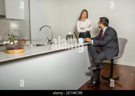 arabo uomo in formalware che lavora nel suo computer e la sua donna essere infastiditi sullo sfondo in una cucina Foto Stock