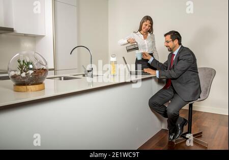 coppia in cucina con l'uomo woking nel suo laptop e donna che lo serviva caffè Foto Stock