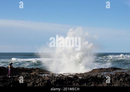 Una coppia che guarda un'enorme onda che si schiantano sulla costa rocciosa vicino a Yachats, Oregon. Foto Stock