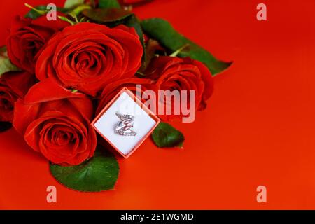 Anello di fidanzamento e bella rosa rossa su sfondo rosso. San Valentino. Foto Stock