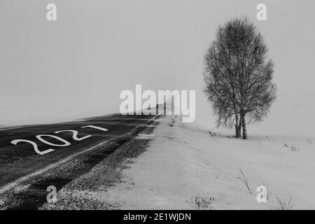 Un'auto con i fari accesi si muove da lontano lungo l'autostrada in nebbia. Nuovi inizi nel 2021 Foto Stock