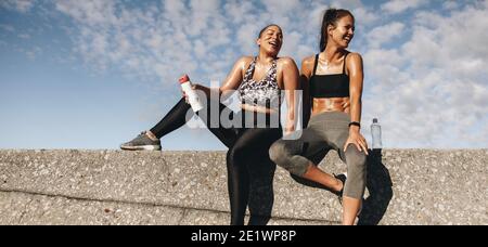 donne in forma fisica che riposano dopo l'allenamento. Due donne sedute all'aperto dopo una sessione di allenamento e sorridenti. Foto Stock