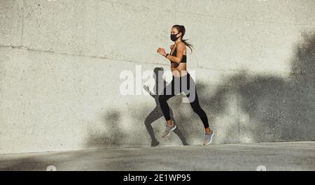 Donna in una corsa mattutina. Donna in forma fisica indossare maschera viso che si sprint all'aperto. Foto Stock