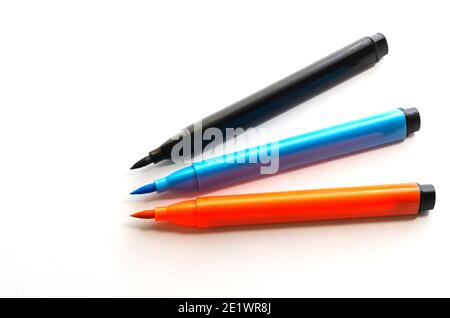 Tre nuovi pennarello multicolore su sfondo bianco. Penne in feltro nere, arancioni e blu per la verniciatura senza tappi. Primo piano, messa a fuoco selettiva Foto Stock